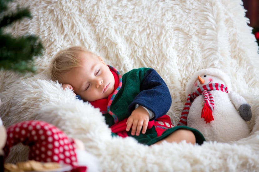 Baby boy, cute child, wearing santa claus robe sitting in rocking chair with Christmas tree and ligh...