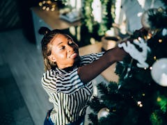 A happy woman in a black and white striped shirt decorates her Christmas tree while listening to mus...