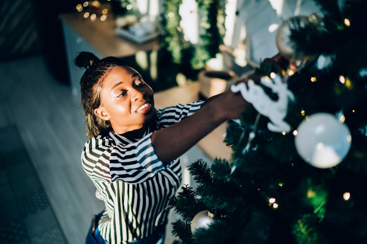 A happy woman in a black and white striped shirt decorates her Christmas tree while listening to mus...