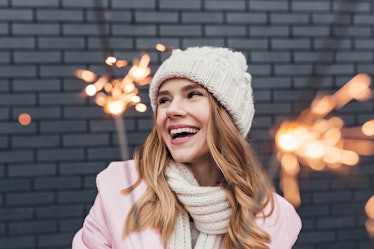 Happy cute girl in winter hat posing with sparkler. Outdoor shot of interested blonde woman having f...