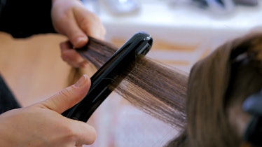 Professional hairdresser, stylist doing hairstyle and using straightener on beautiful long hair of c...