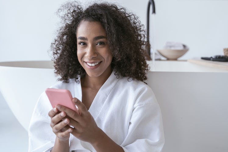 Beautiful smiling woman sitting in the bathroom with a smartphone in her hands