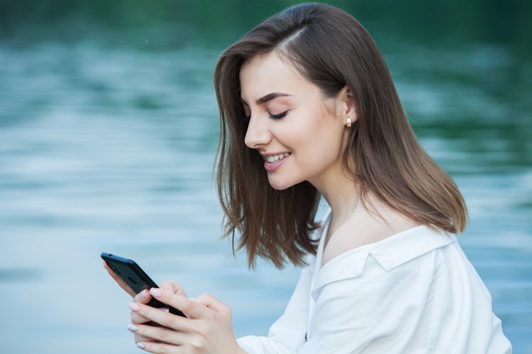 Girl outdoors texting on her mobile phone. Girl with phone. Portrait of a happy woman text sms messa...