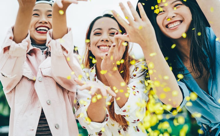 Three happy friends throw yellow flower petals in the air on a spring day.