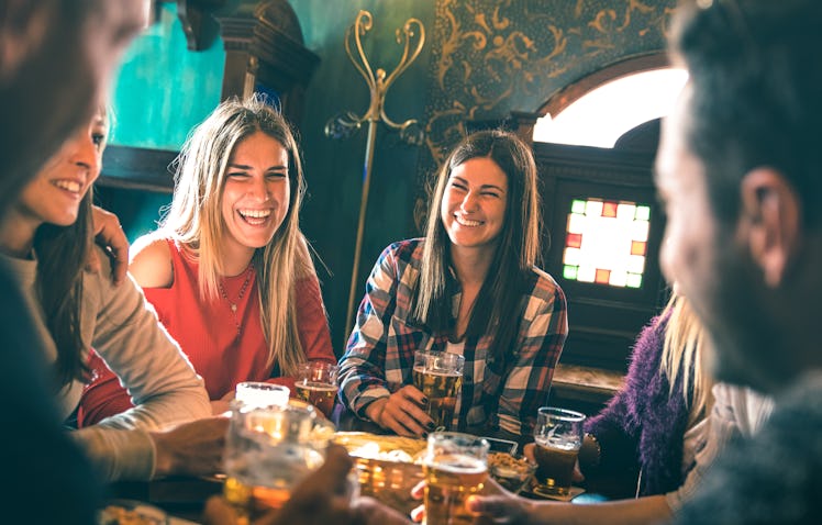 A group of happy friends, with two women smiling in the center, drink beer at a beer hall. 