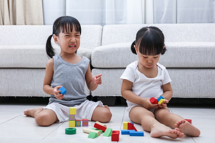 Asian Chinese little sisters struggle for blocks on the floor in the living room at home.