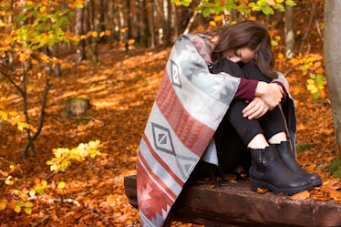 young brunette woman sitting outside in autumn and is sad