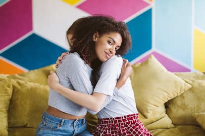 Young pretty african american woman with dark curly hair hugging girlfriend dreamily looking in came...