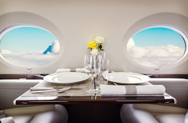 Luxury interior in bright colors of genuine leather in the business jet, sky and clouds through the ...