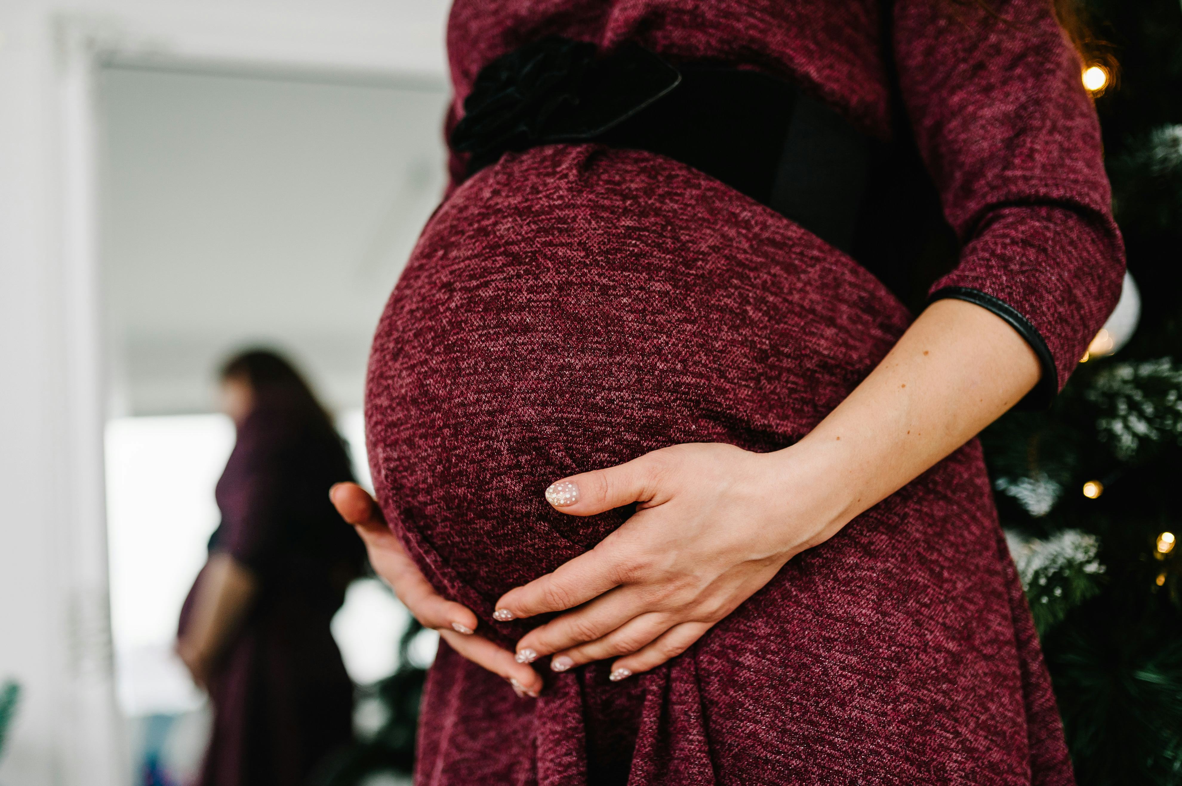 Cropped photo of pregnant woman in a red dress stands near the Christmas tree. Happy New Year and Me...