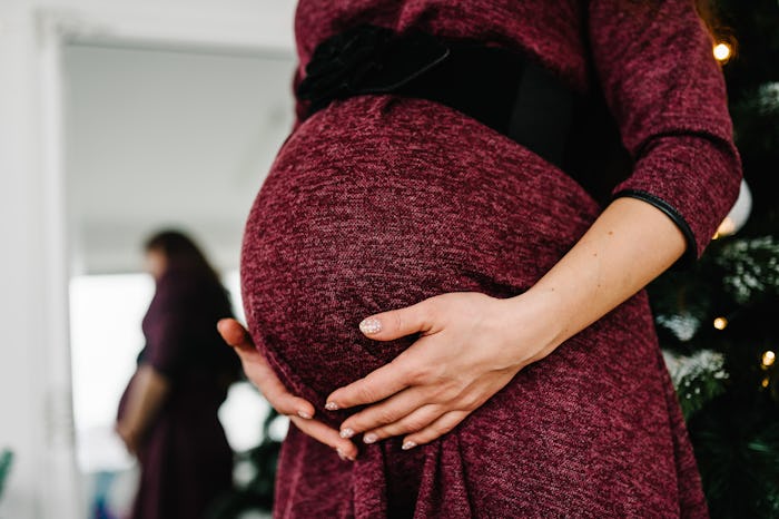 Cropped photo of pregnant woman in a red dress stands near the Christmas tree. Happy New Year and Me...