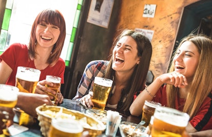 A group of friends laugh while drinking beer at a beer hall table.