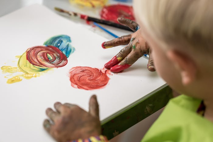 Over the shoulder view of a little boy having fun painting with fingers with colourful hand paints.