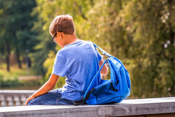 Young boy with a backpack sits by himself outside.