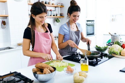 Two brunette women cook and slice potatoes to make mashed potatoes in the kitchen.