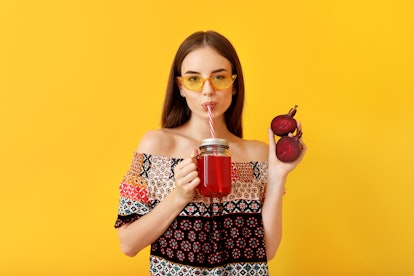 Young woman drinking healthy beet juice on color background