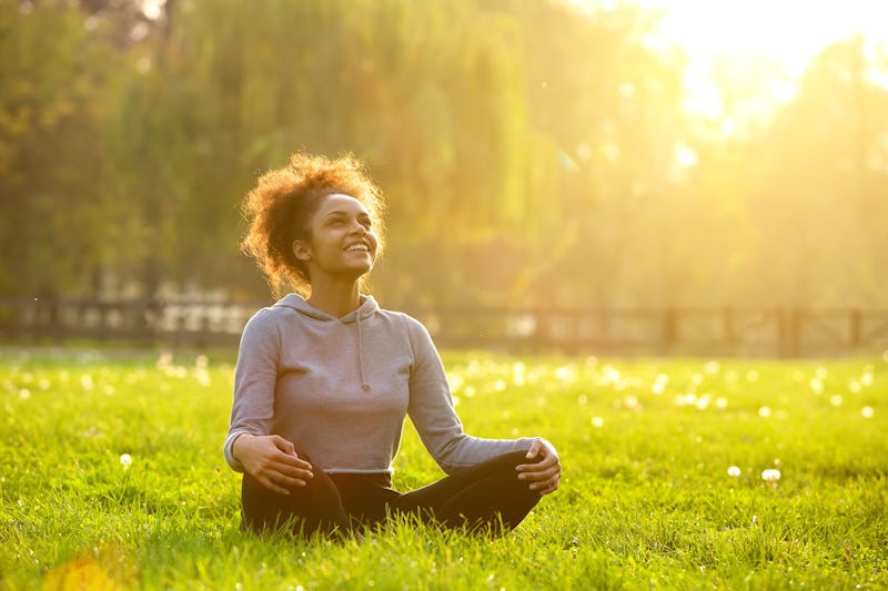 Happy young woman sitting outdoors in yoga position