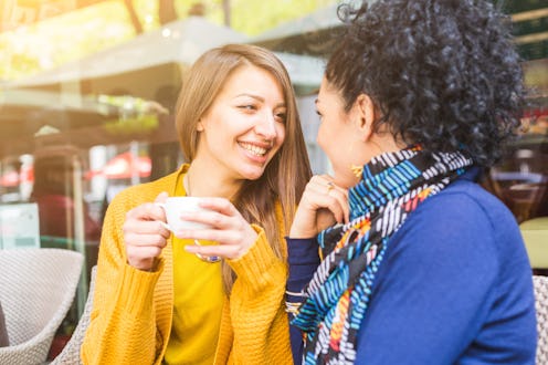 Lesbian couple talking and cuddling at a cafe. Two beautiful young women, sitting next each other a...