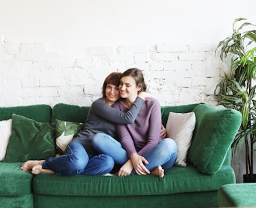 A mother and daughter sit on a green, velvet couch to watch holiday movies.
