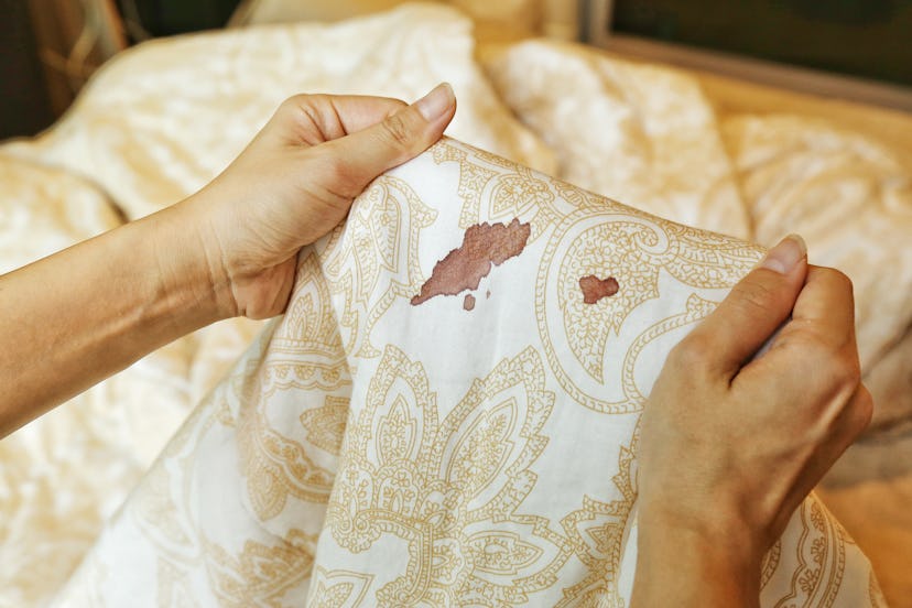 Women's hands hold bed sheet with period blood spot stains. If you've ever wondered how to delay you...