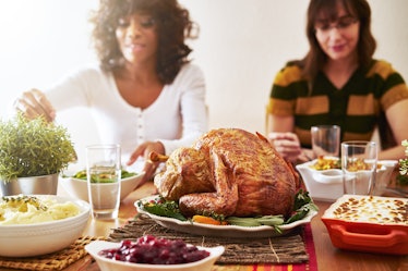 A Thanksgiving dinner spread with turkey, mashed potatoes, cranberry sauce, and people eating in the...