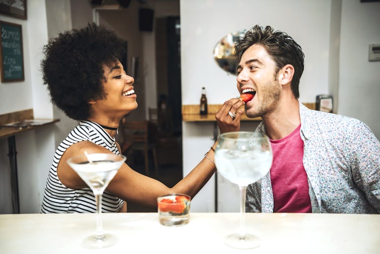 Side view of beautiful woman feeding man with strawberry in bar. 