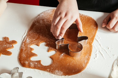 A woman cuts out gingerbread cookies from rolled-out dough in a kitchen.