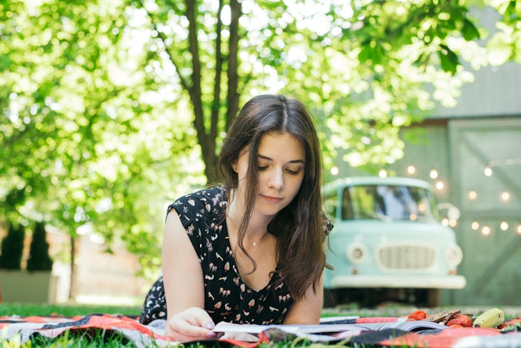 Beautiful young girl resting on a picnic in the summer. She spread the blanket on the grass and lay ...