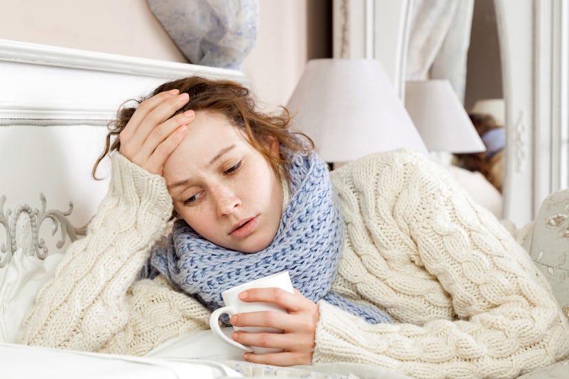 Sick woman with cup of tea. Closeup image of young frustrated sick woman in knitted blue scarf holdi...