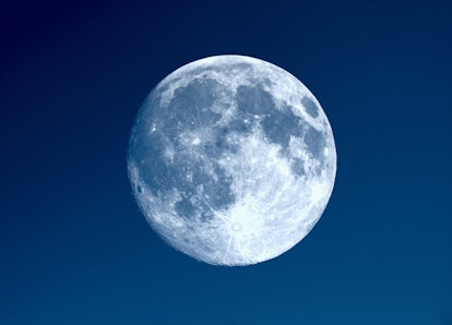 Full moon seen with an astronomical telescope over blue sky