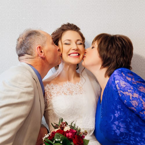 Parents kiss their smiling daughter on her wedding day.