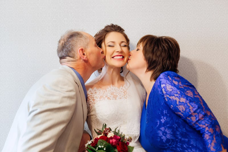 Parents kiss their smiling daughter on her wedding day.