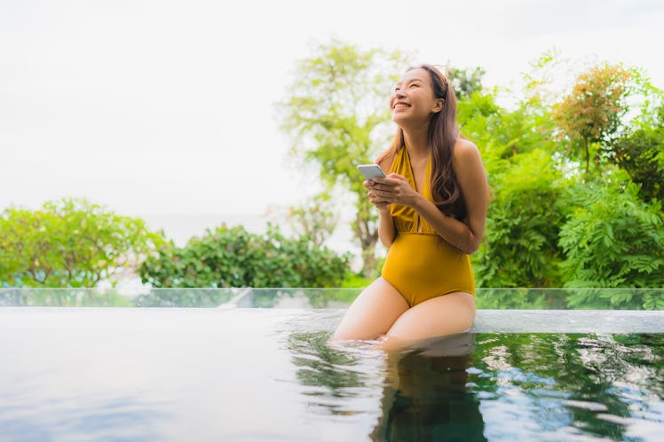 Portrait beautiful young asian woman with cell phone or mobile phone around swimming pool at hotel r...