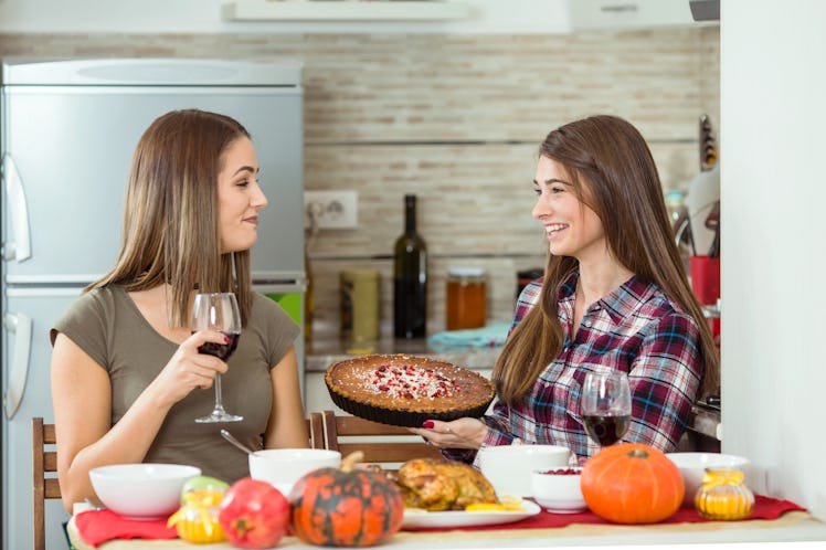 Two smiling sisters in the kitchen look at each other, while one holds a glass of red wine and the o...