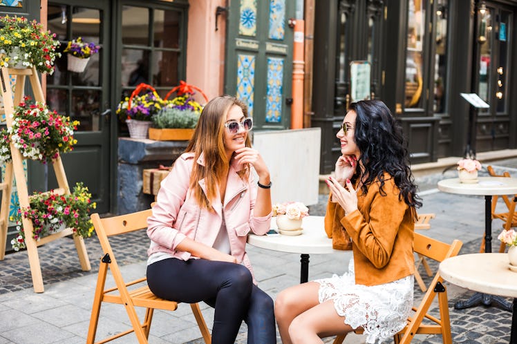 Two stylish friends sit at an outdoor restaurant in the city for Thanksgiving brunch.