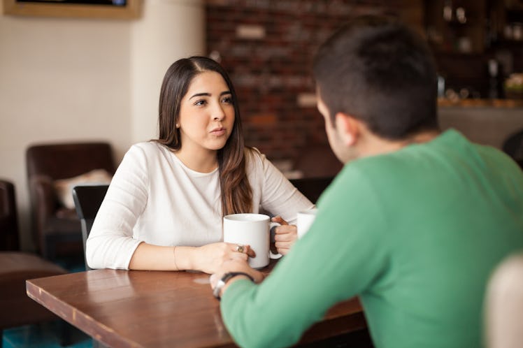 Cute young brunette drinking some coffee while talking with a male friend at a cafe