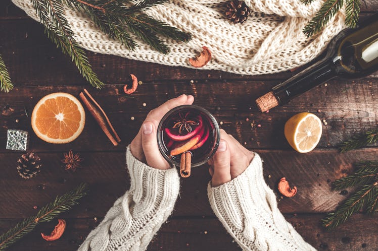 A woman's hands hold a mug of mulled wine on a table with winter decor.