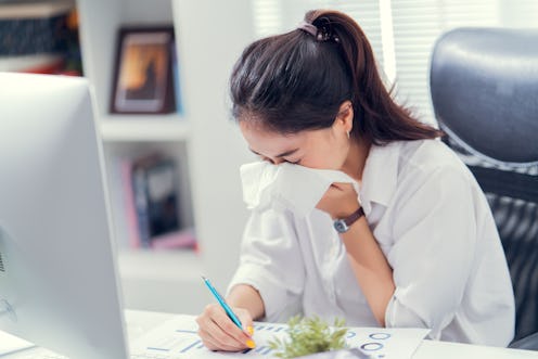 Women are sneezing and are cold. She is in the office.