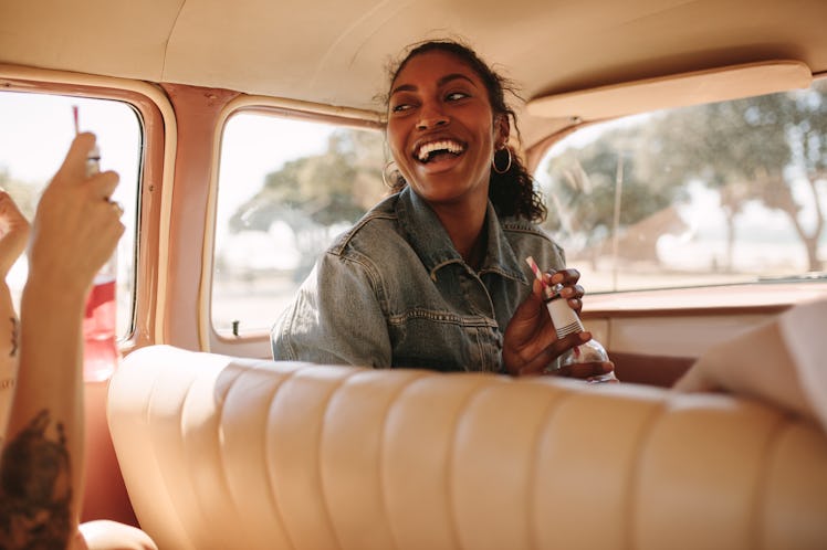 A woman laughs in a car while on a road trip with her friends.