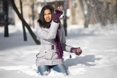 Beautiful smiling american black female sitting in the snow outdoors playing with snow