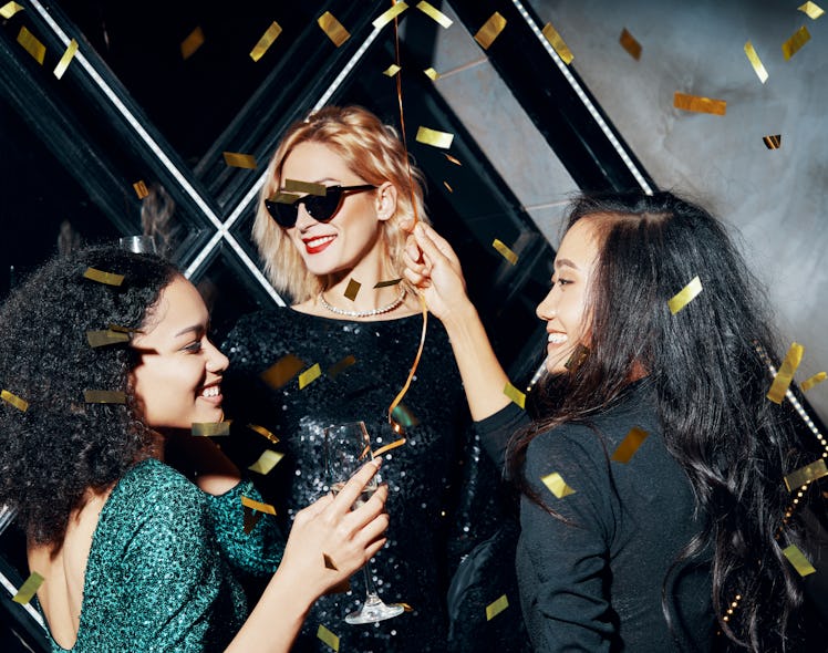 Pretty multiethnic young women have fun together celebrating with confetti on party. Friendship and...
