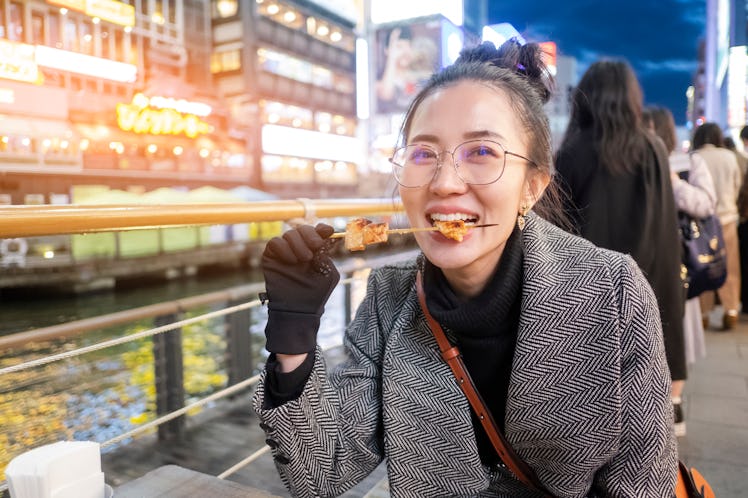 Young woman tourists enjoy eating street food in walking at street shopping center Dotonbori in Osak...