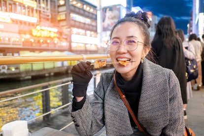 Young woman tourists enjoy eating street food in walking at street shopping center Dotonbori in Osak...