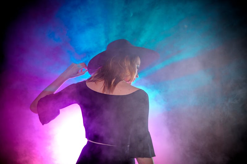 Witch/Wiccan Fashion inspired model with a wide brimmed black hat and black clothing. Shot with a LED lighting array for high color contrast and with theatrical fog. Model against a black background