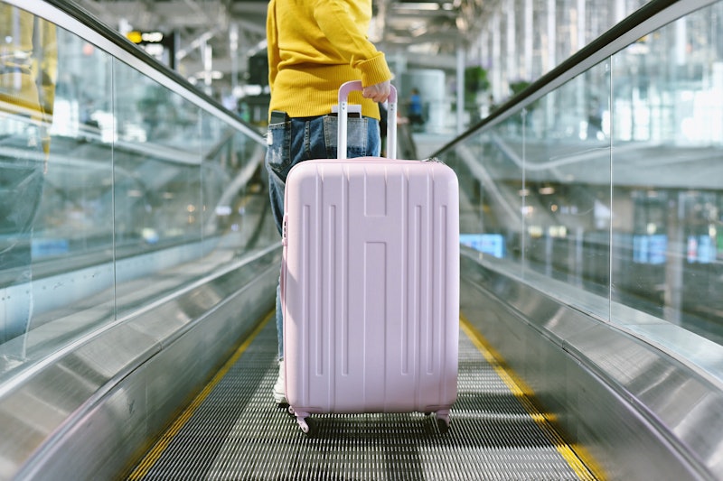 Woman traveler carry big suitcase on escalator walkway at the airport terminal, Passenger walking wi...