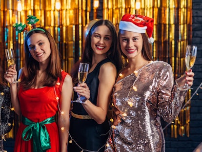 A group of girls smile and pose in front of a shiny gold backdrop dressed in festive attire for Sant...