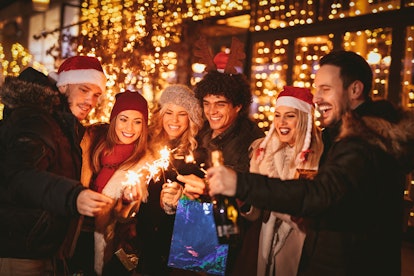 A group of friends laugh with sparklers and champagne at a Christmas party outside.