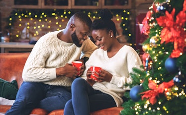Celebrating Christmas together. Young african couple holding red mugs, reading coffee grounds to lea...