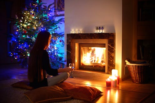 Woman having a drink by a fireplace in a cozy dark living room on Christmas eve