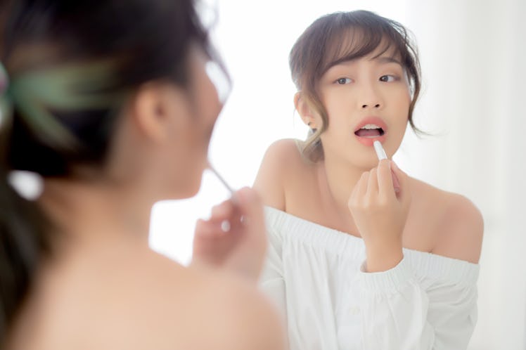 Beautiful portrait young asian woman looking mirror applying makeup lipstick at room, beauty lips as...